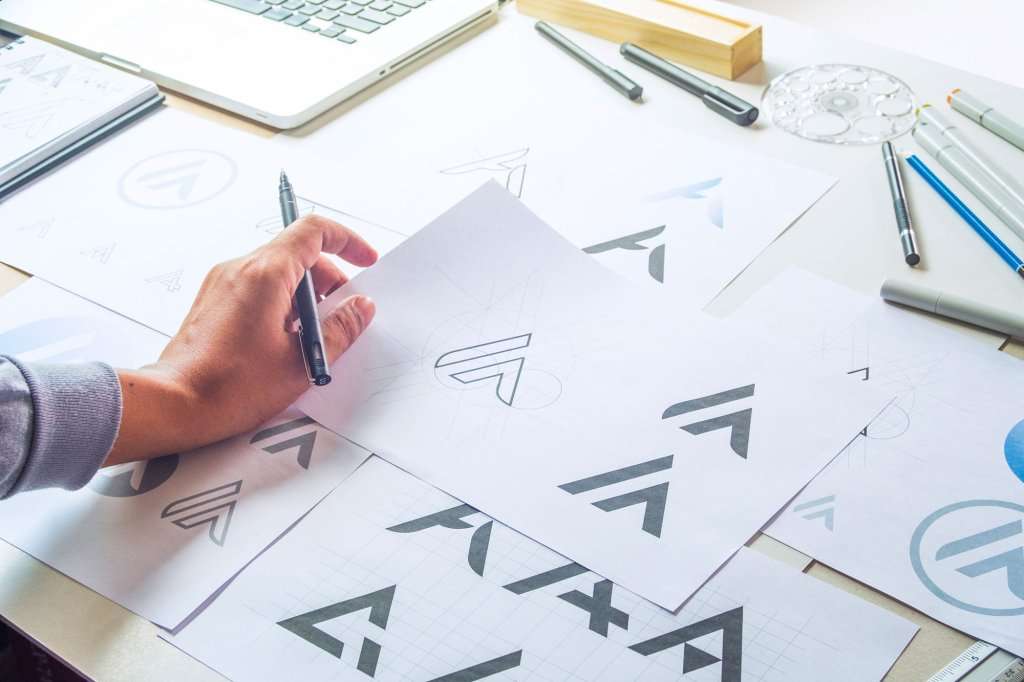 A designer's hand sketching logo concept variations on paper at a desk